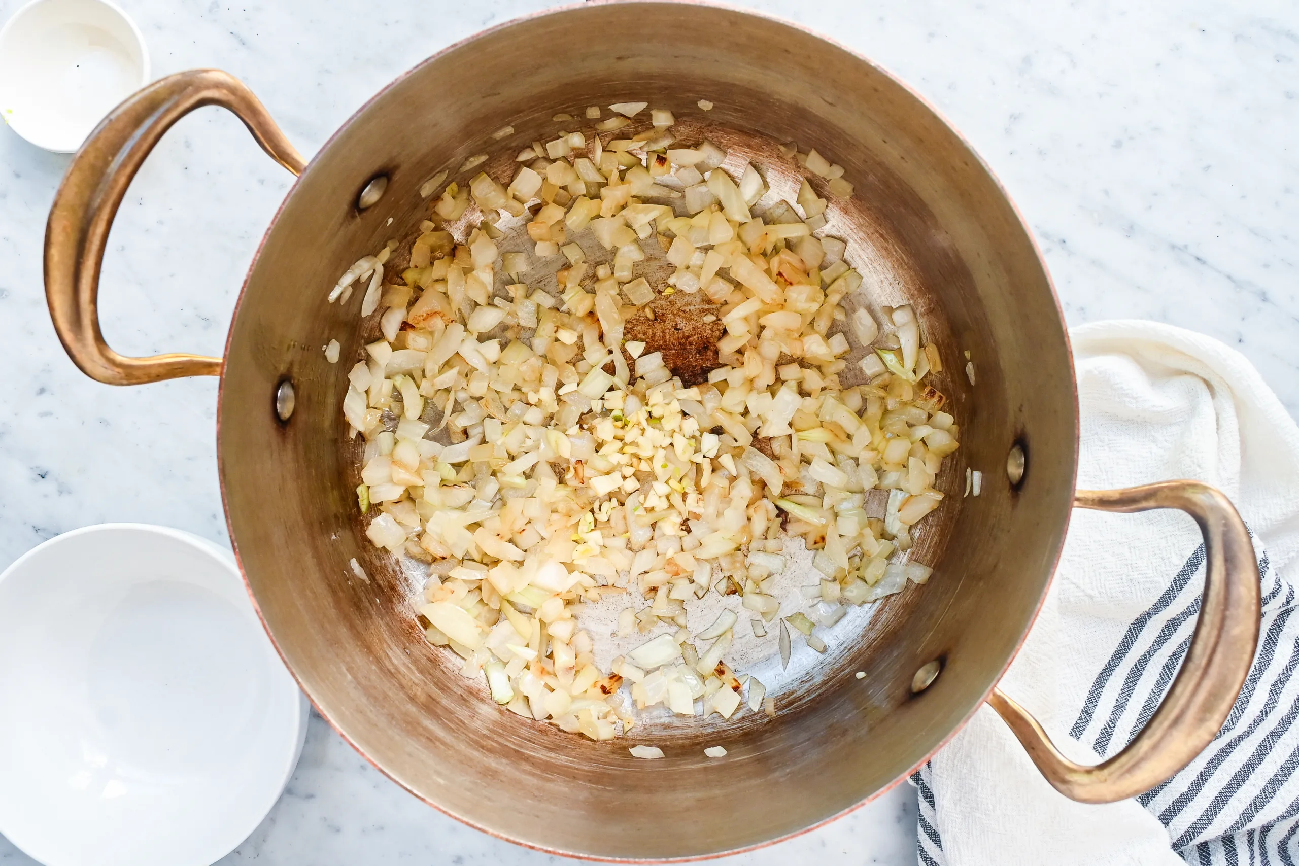 Chopped garlic added to softened onions in a copper pot.