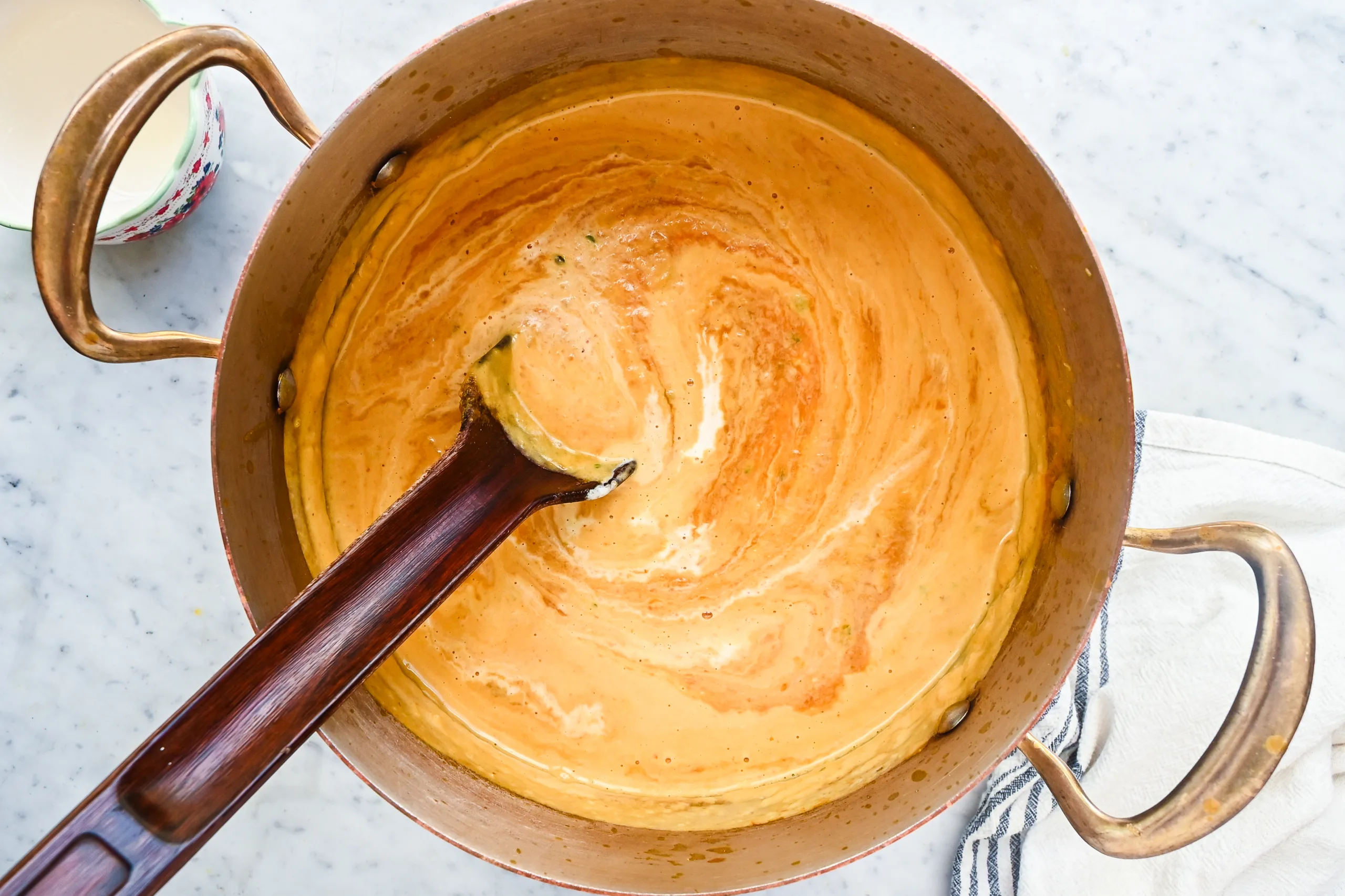 Cream stirred into pumpkin soup in a copper pot.