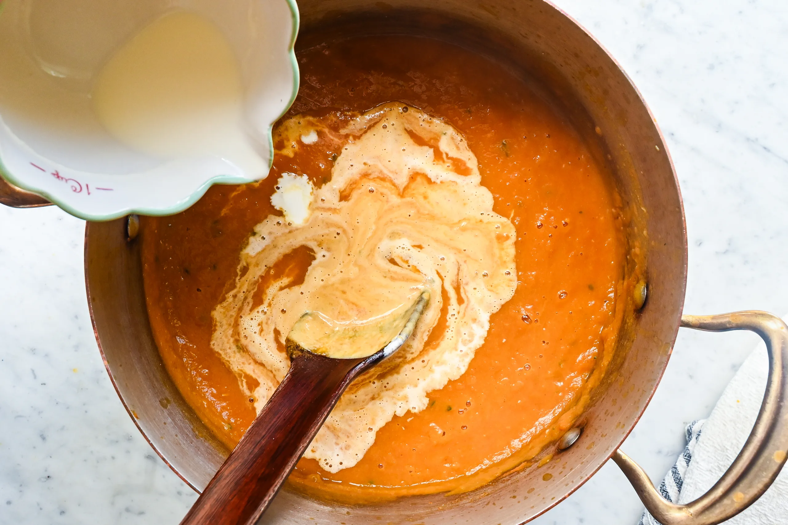 Heavy cream being poured into blended pumpkin soup.