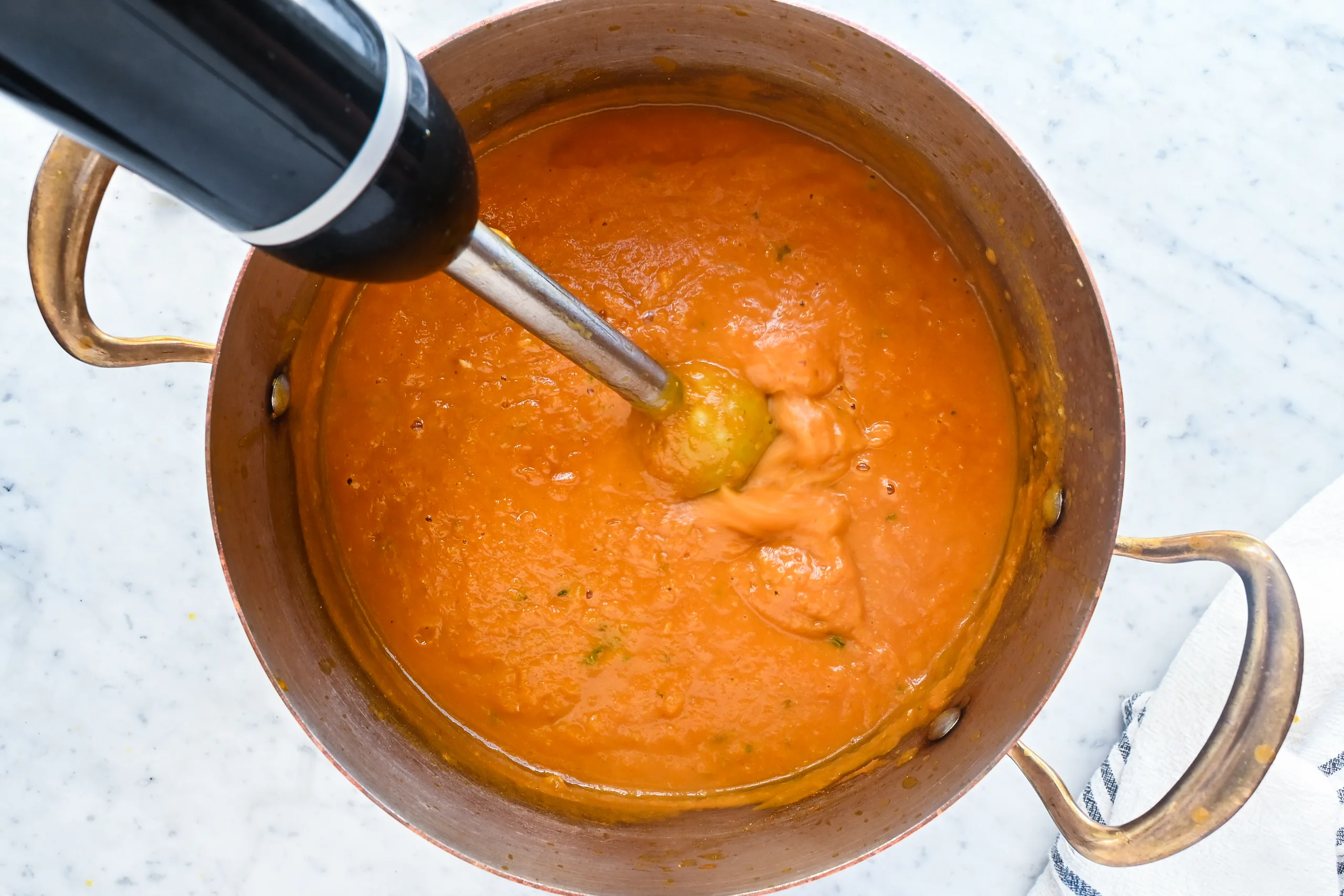 Pumpkin soup being blended with an immersion blender in a copper pot.