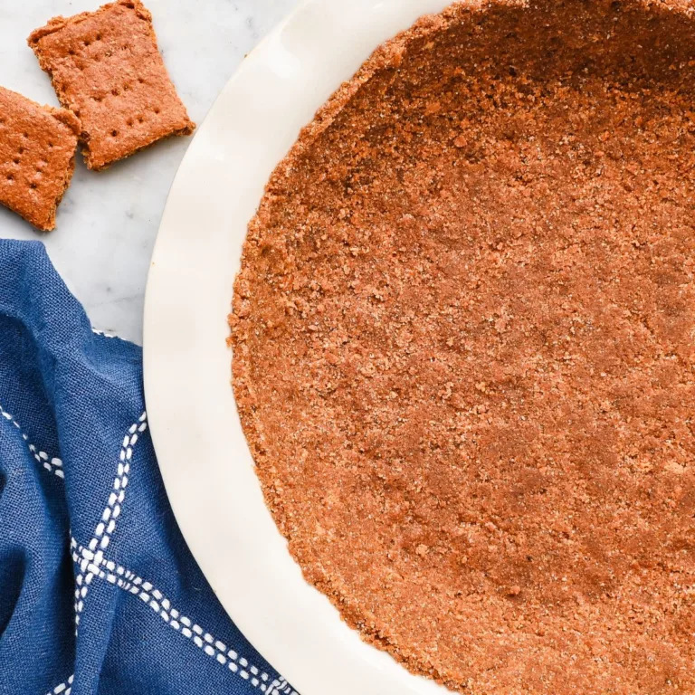 Homemade graham cracker pie crust pressed into a white pie plate with graham crackers and a blue towel nearby.