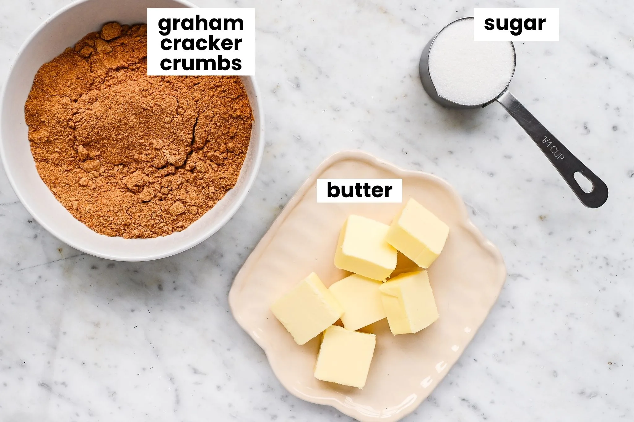 Graham cracker pie crust ingredients arranged on a marble counter, including graham cracker crumbs, sugar, and butter.