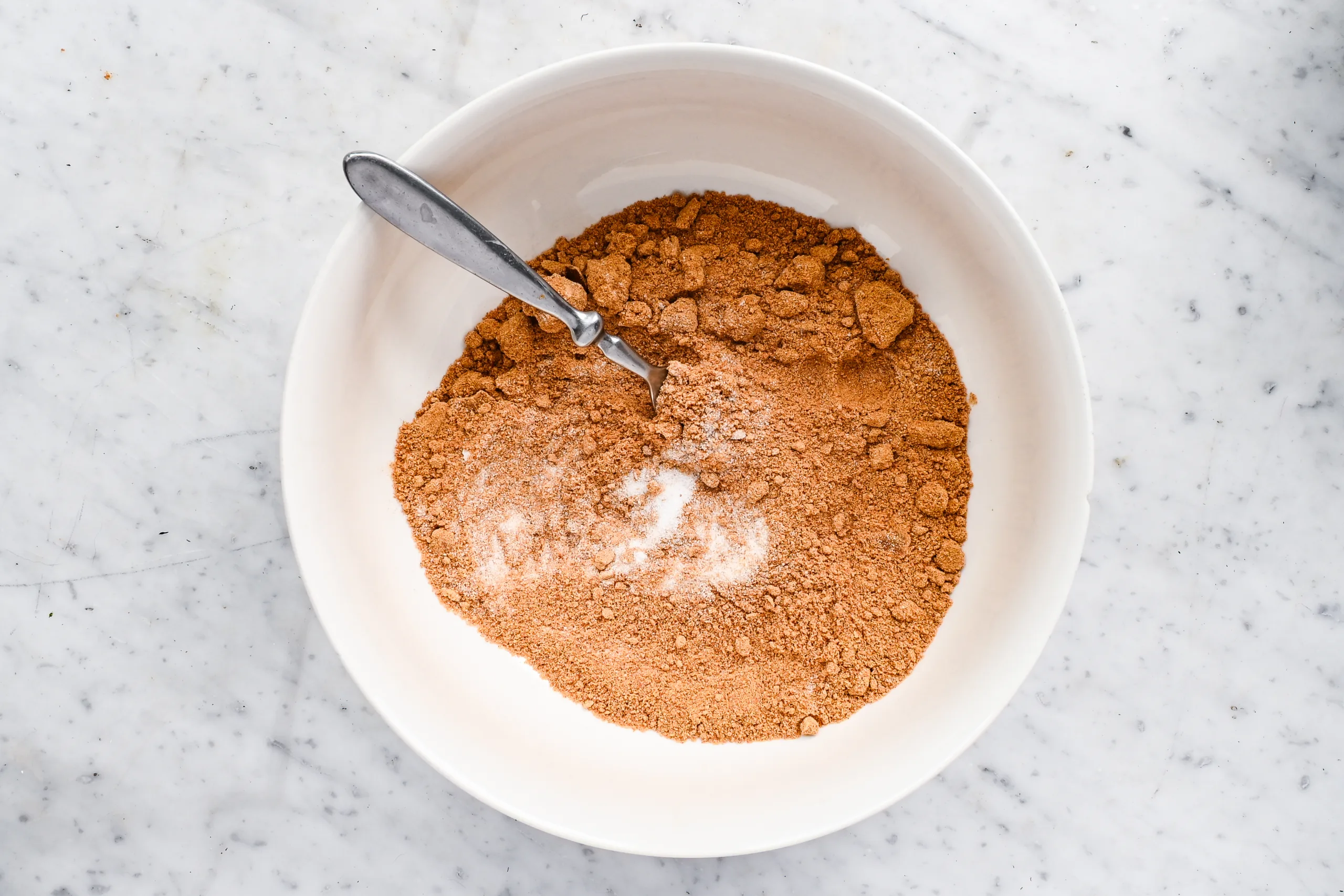 Graham cracker crumbs and sugar in a white mixing bowl with a fork.
