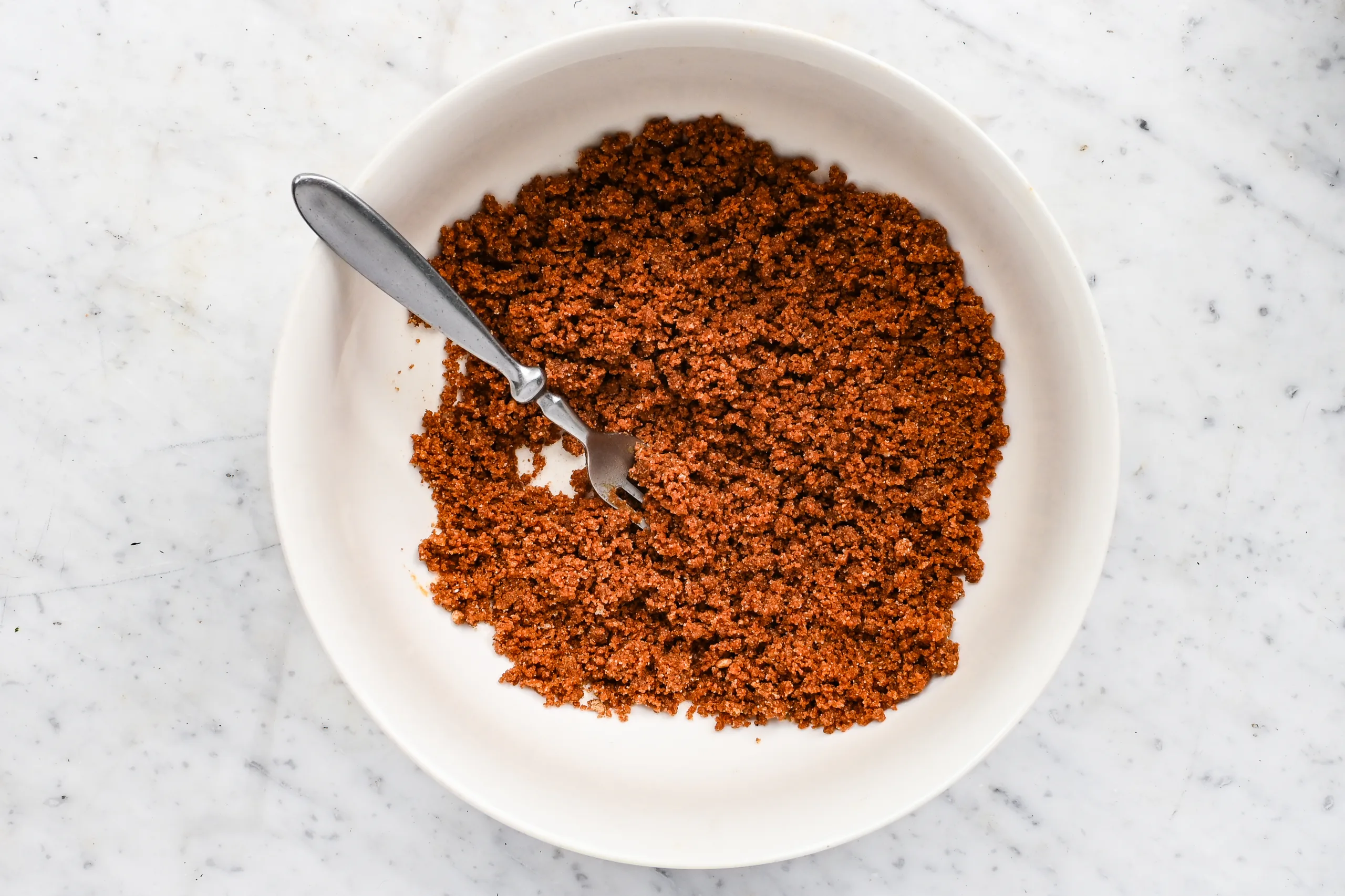 Graham cracker crumb mixture stirred with melted butter in a white mixing bowl.
