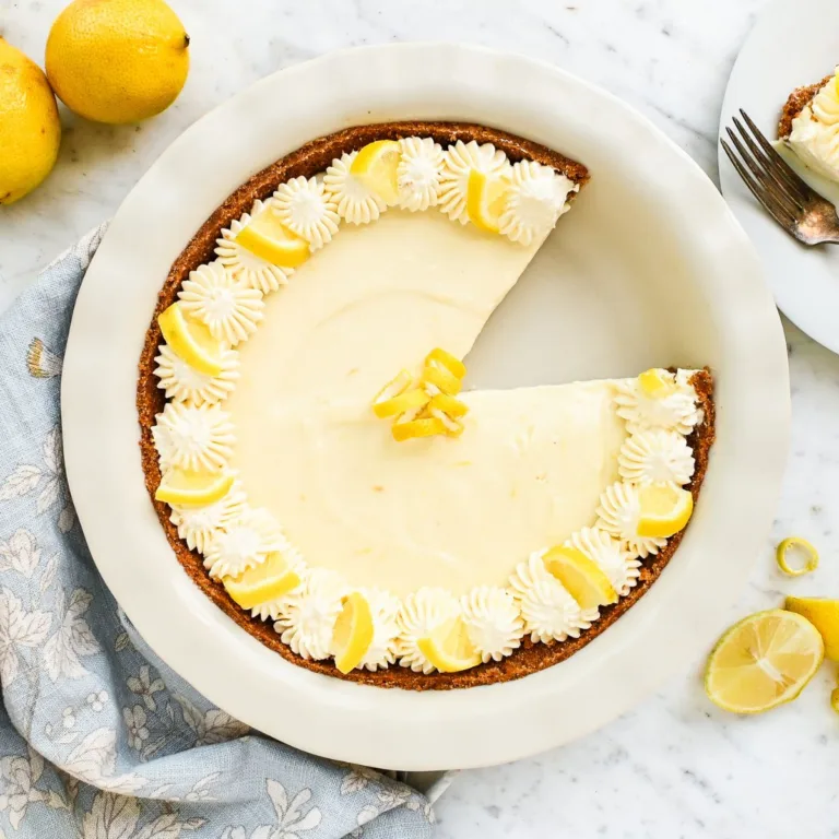 No-bake lemon icebox pie in a graham cracker crust, decorated with whipped cream rosettes, lemon wedges, and curled lemon zest.
