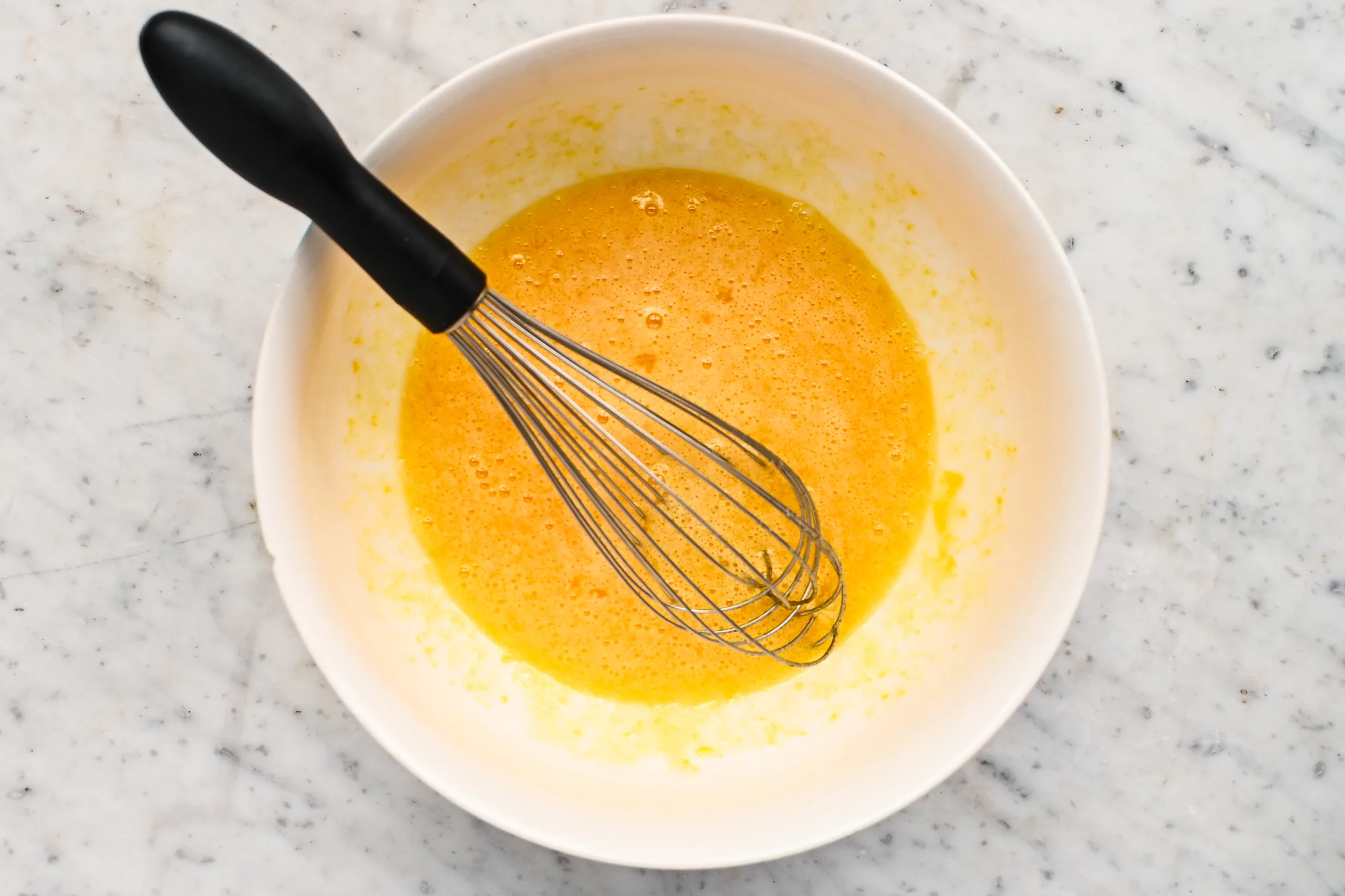 Eggs and sugar whisked together in a white mixing bowl for pumpkin crisp filling.