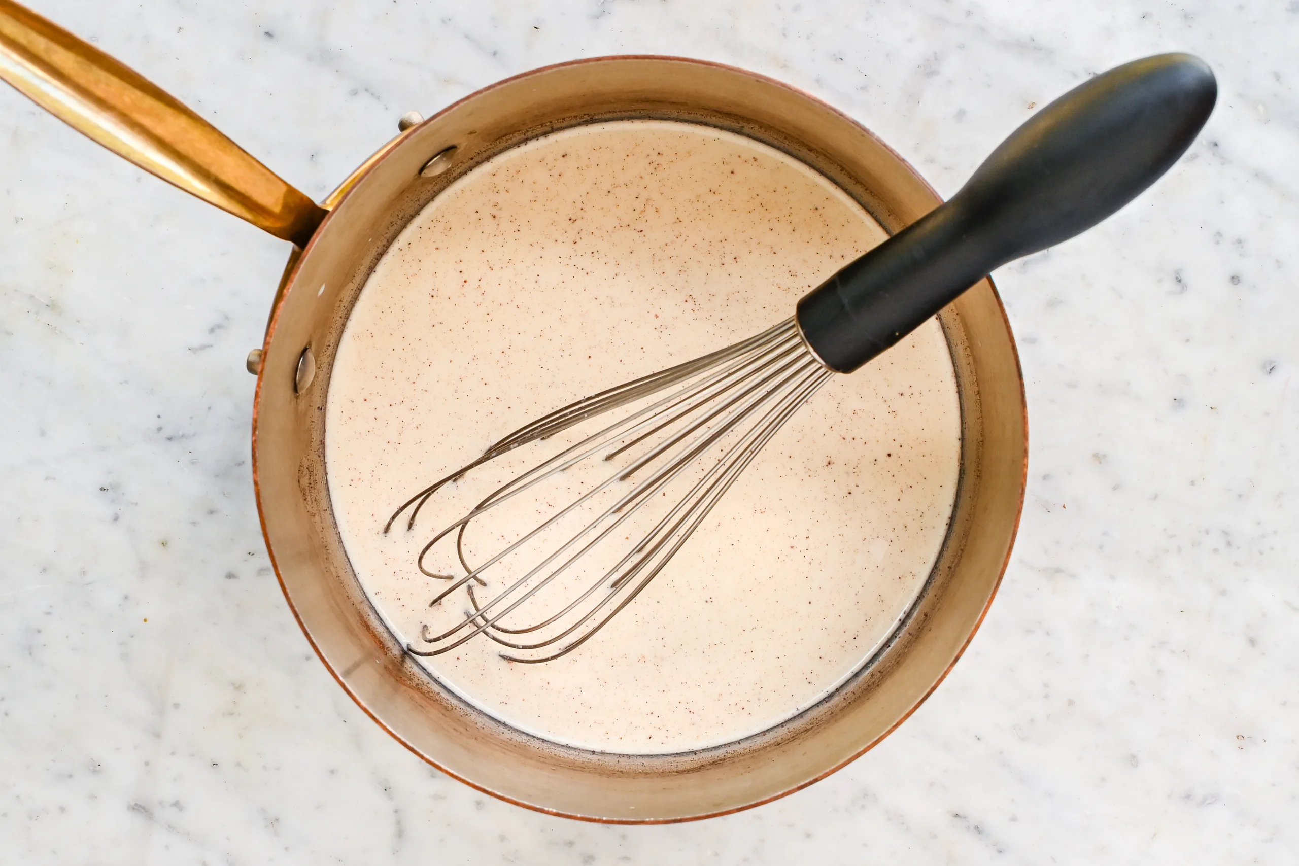 Warm eggnog ice cream custard in a copper saucepan with a whisk.