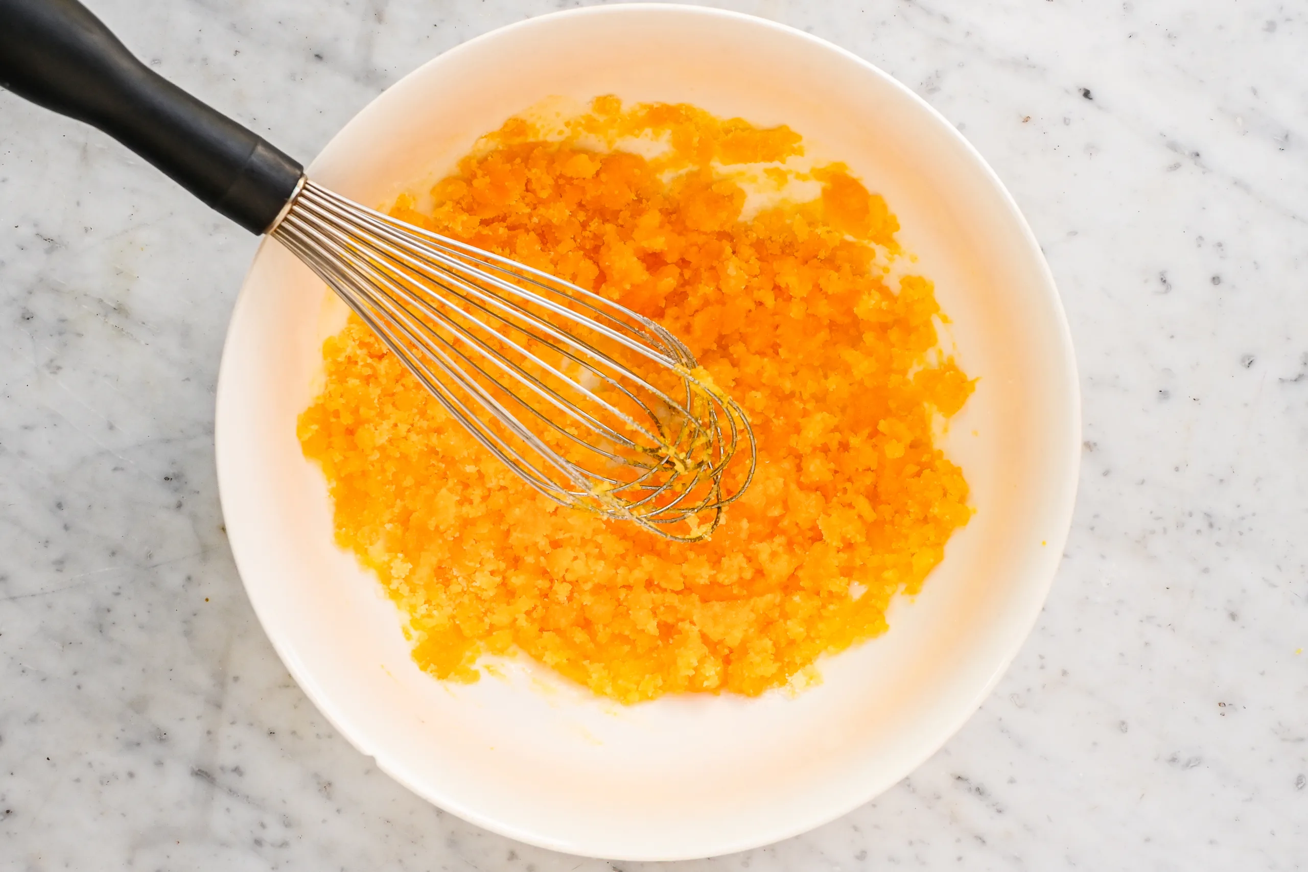 Egg yolks and sugar whisked together in a mixing bowl for eggnog ice cream.