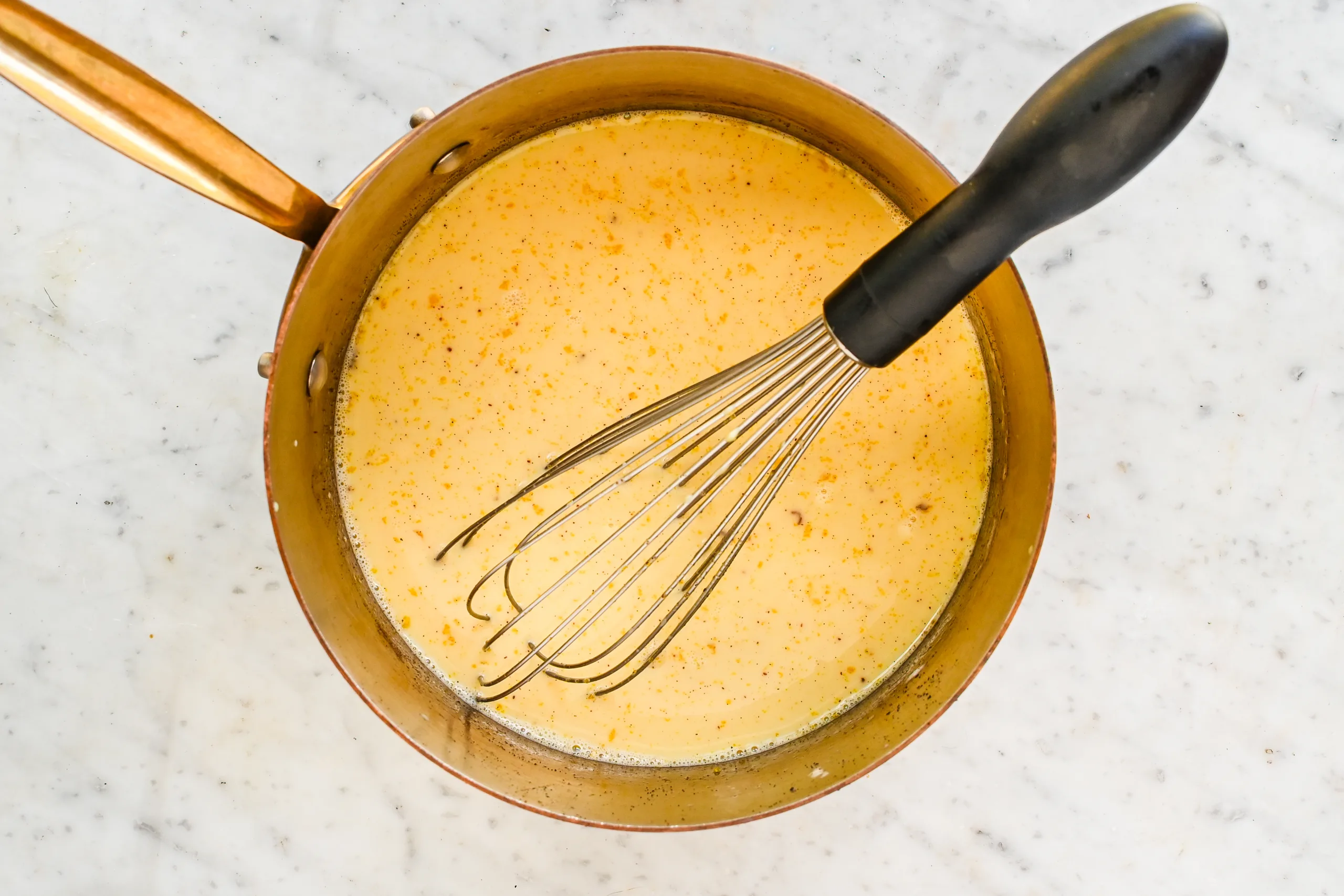 Spiced eggnog ice cream custard in a copper saucepan with a whisk.