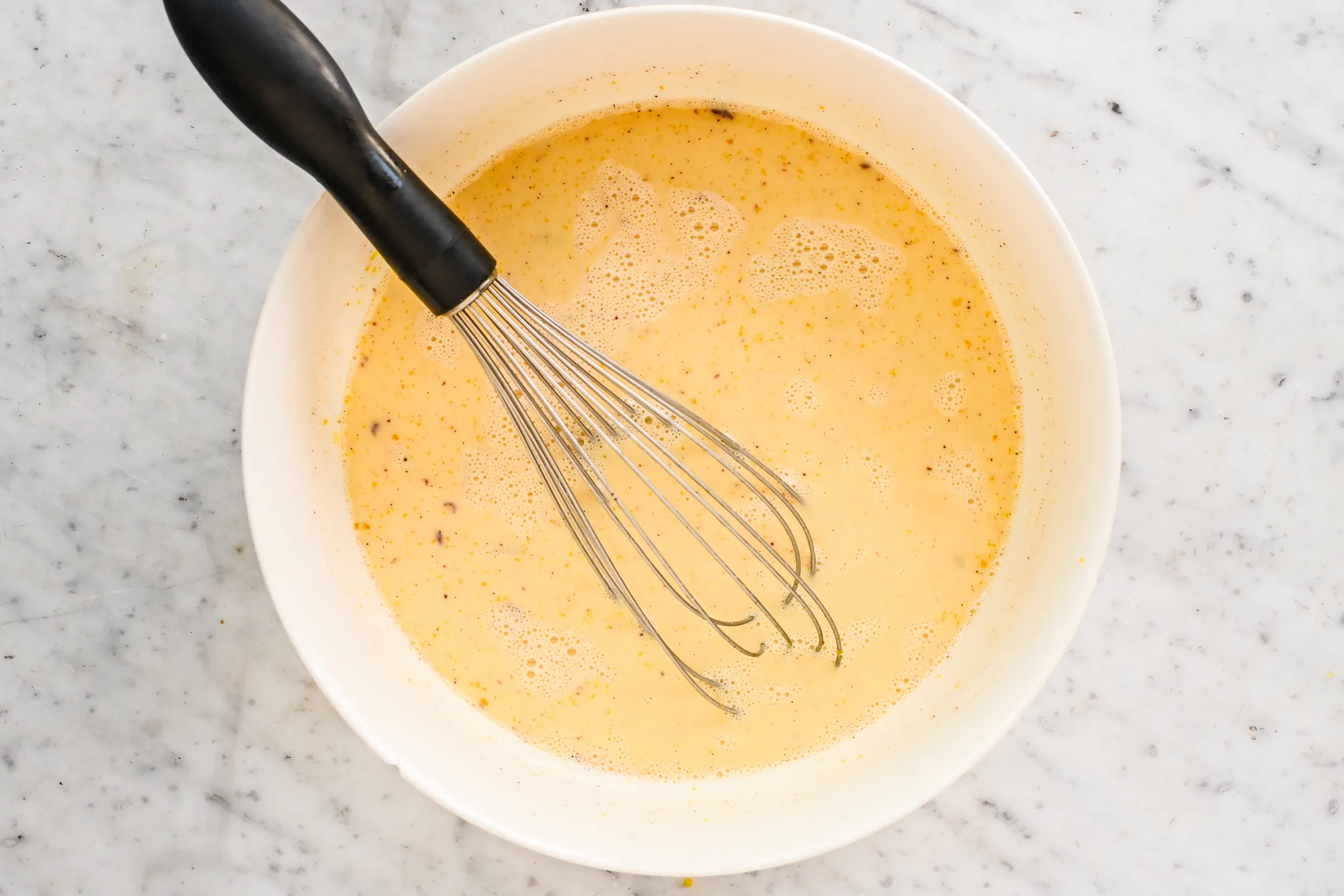 Eggnog ice cream custard mixed in a white bowl with a whisk.