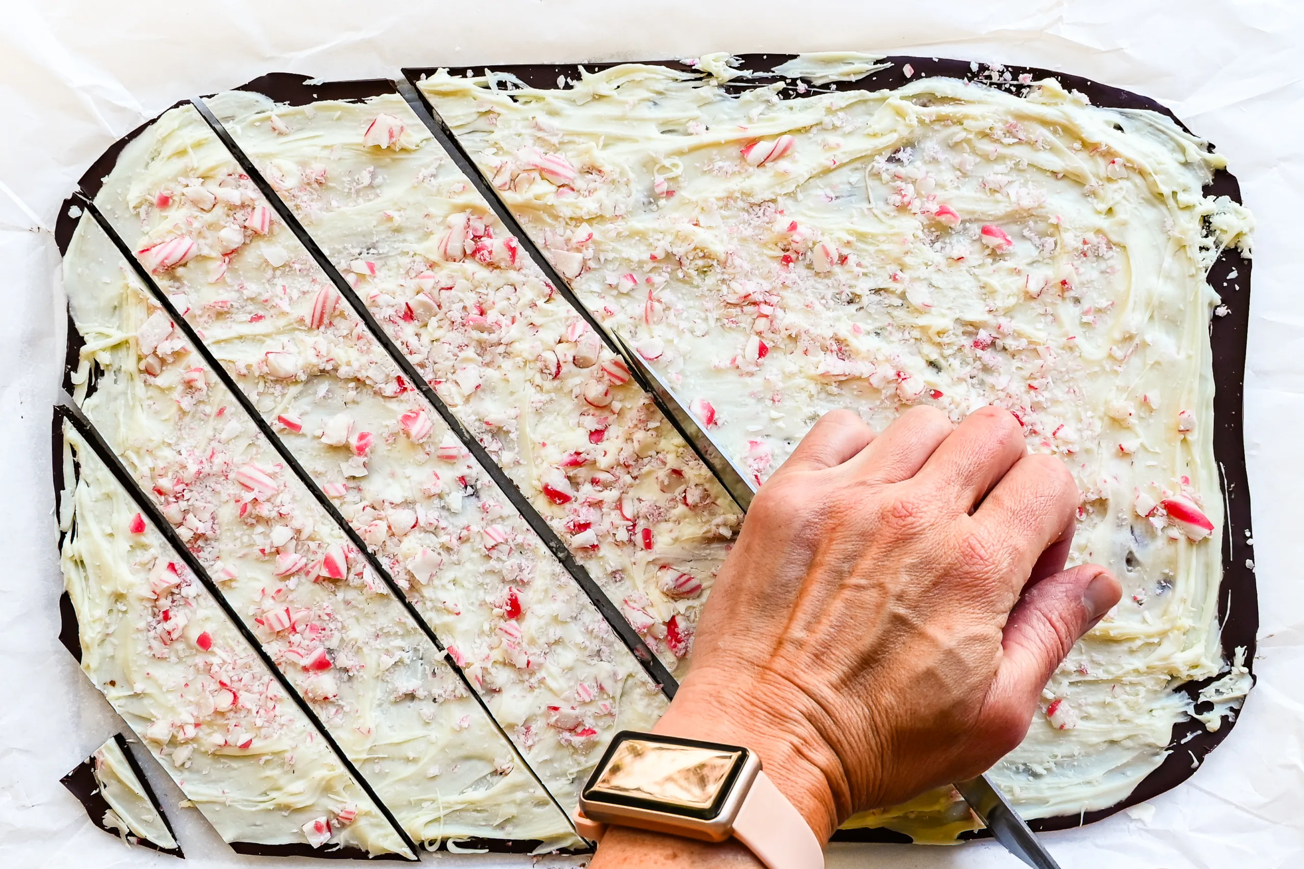 Peppermint bark being cut into long pieces on parchment paper.