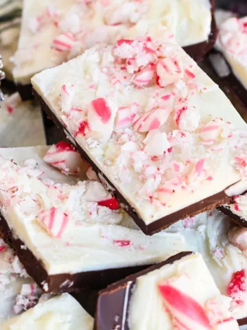 Layered peppermint bark pieces topped with crushed candy canes, with a pine cone and Christmas greenery nearby.