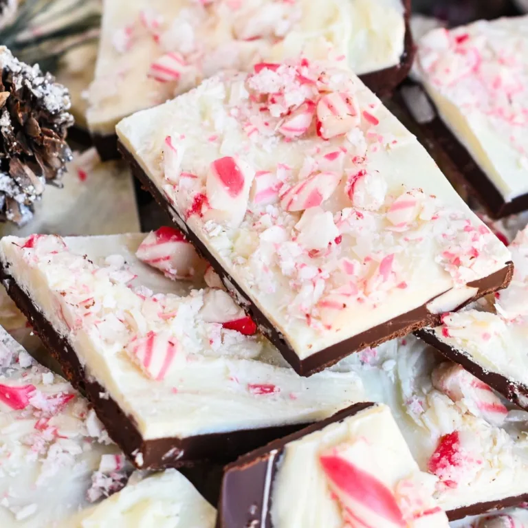 Layered peppermint bark pieces topped with crushed candy canes, with a pine cone and Christmas greenery nearby.