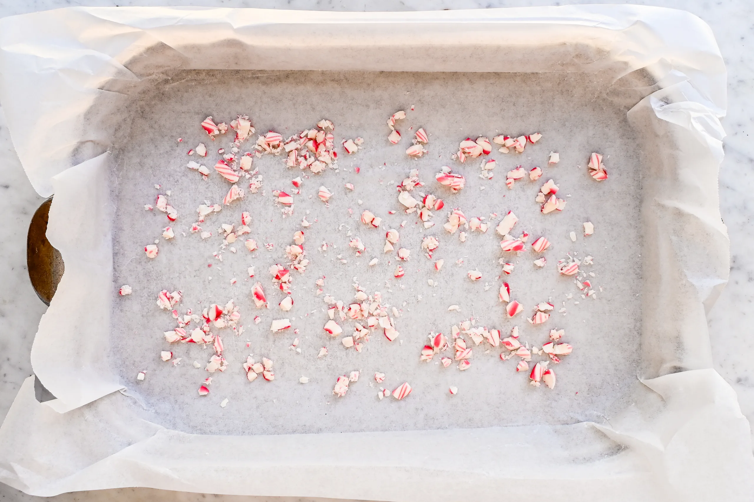 Crushed peppermint candy scattered in a parchment-lined baking pan for peppermint bark.