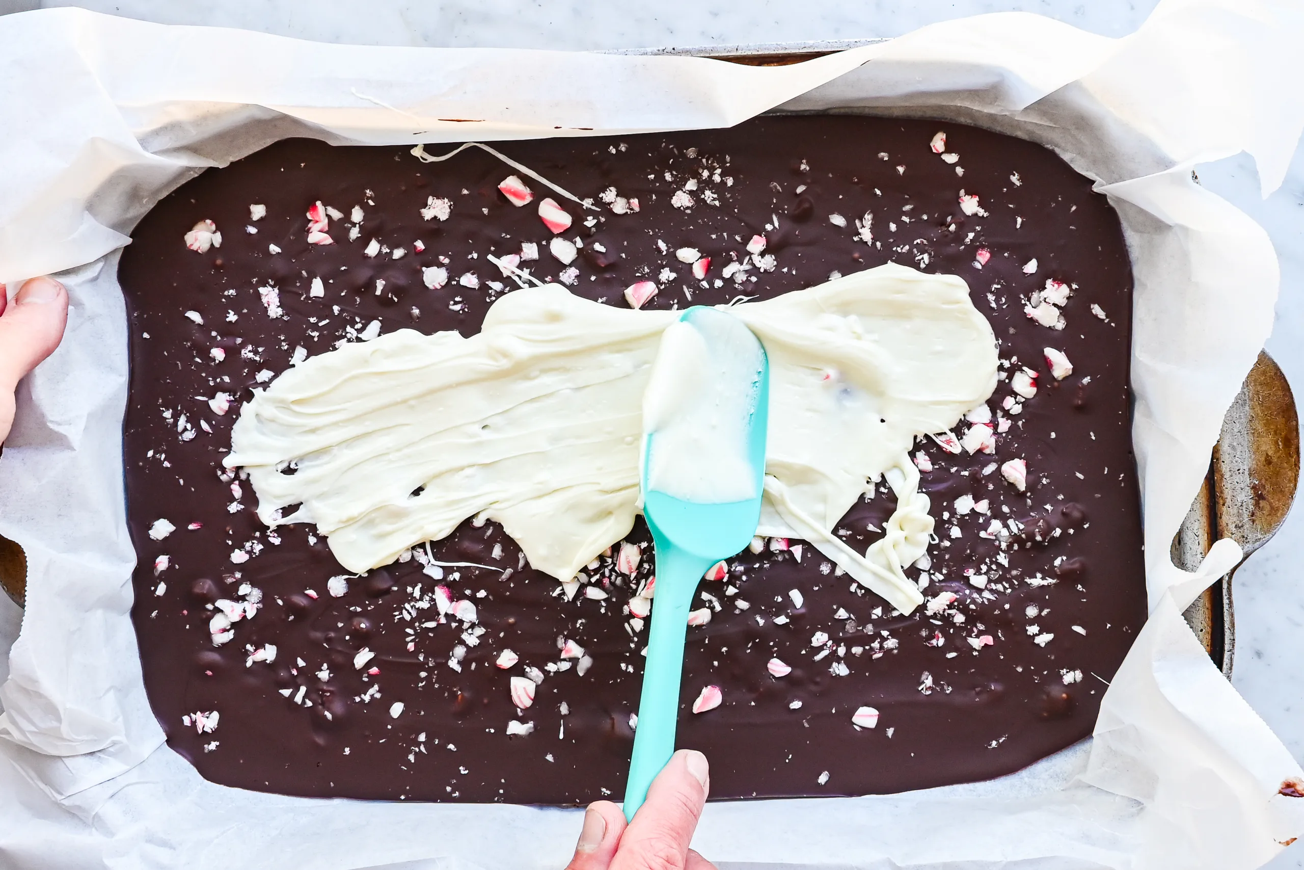 White chocolate being spread over the dark chocolate layer with crushed peppermint candy underneath.