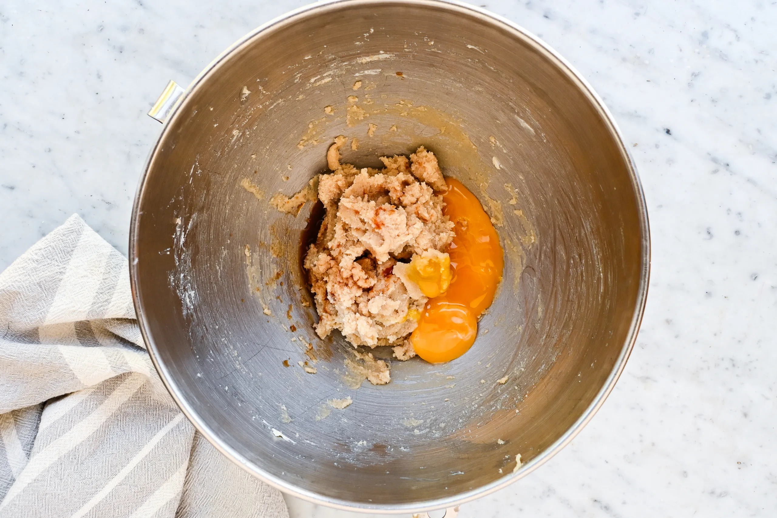 Egg yolks, vanilla extract, and rum extract added to eggnog cookie dough in a stand mixer bowl.