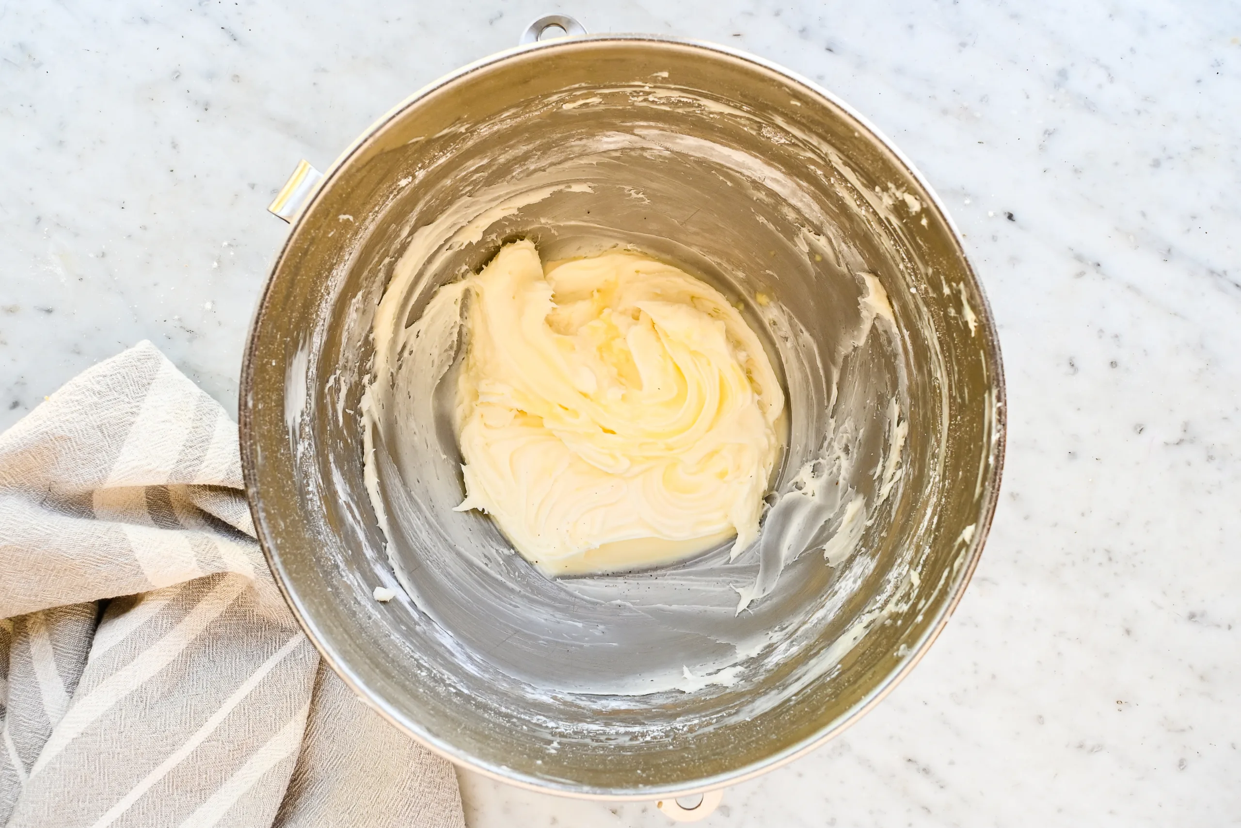 Butter and cream cheese creamed together to make the cream cheese frosting in a stand mixer bowl.
