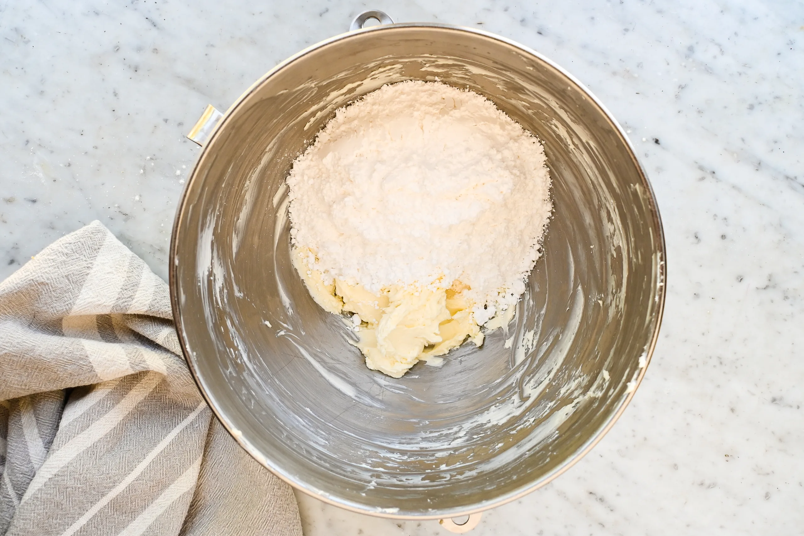 Powdered sugar added to cream cheese and butter in a mixer bowl for eggnog cream cheese frosting.