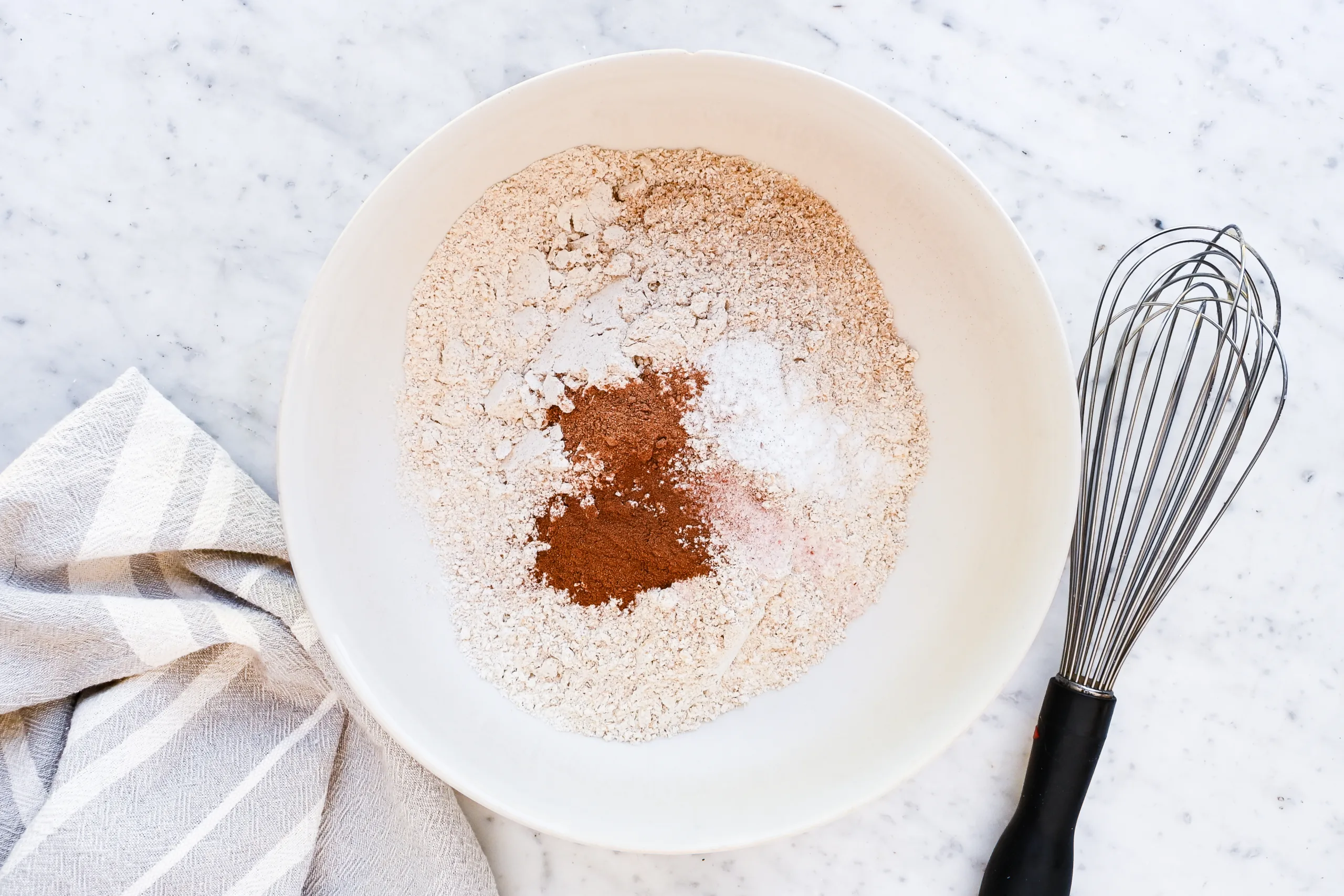 Flour, baking powder, salt, nutmeg, and cinnamon in a mixing bowl for eggnog cookies.
