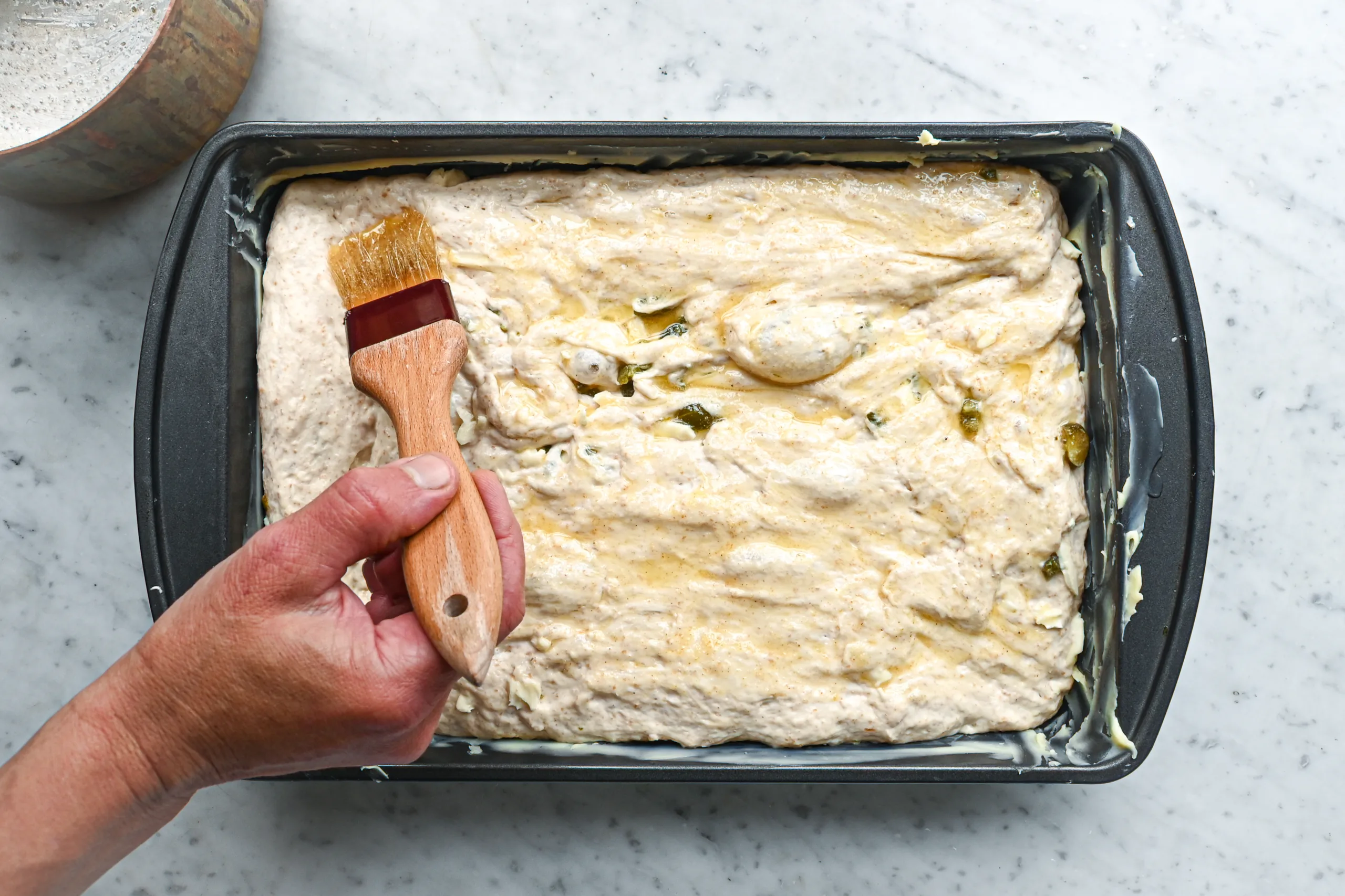 Garlic butter being brushed over jalapeño cheddar sourdough focaccia dough before baking.