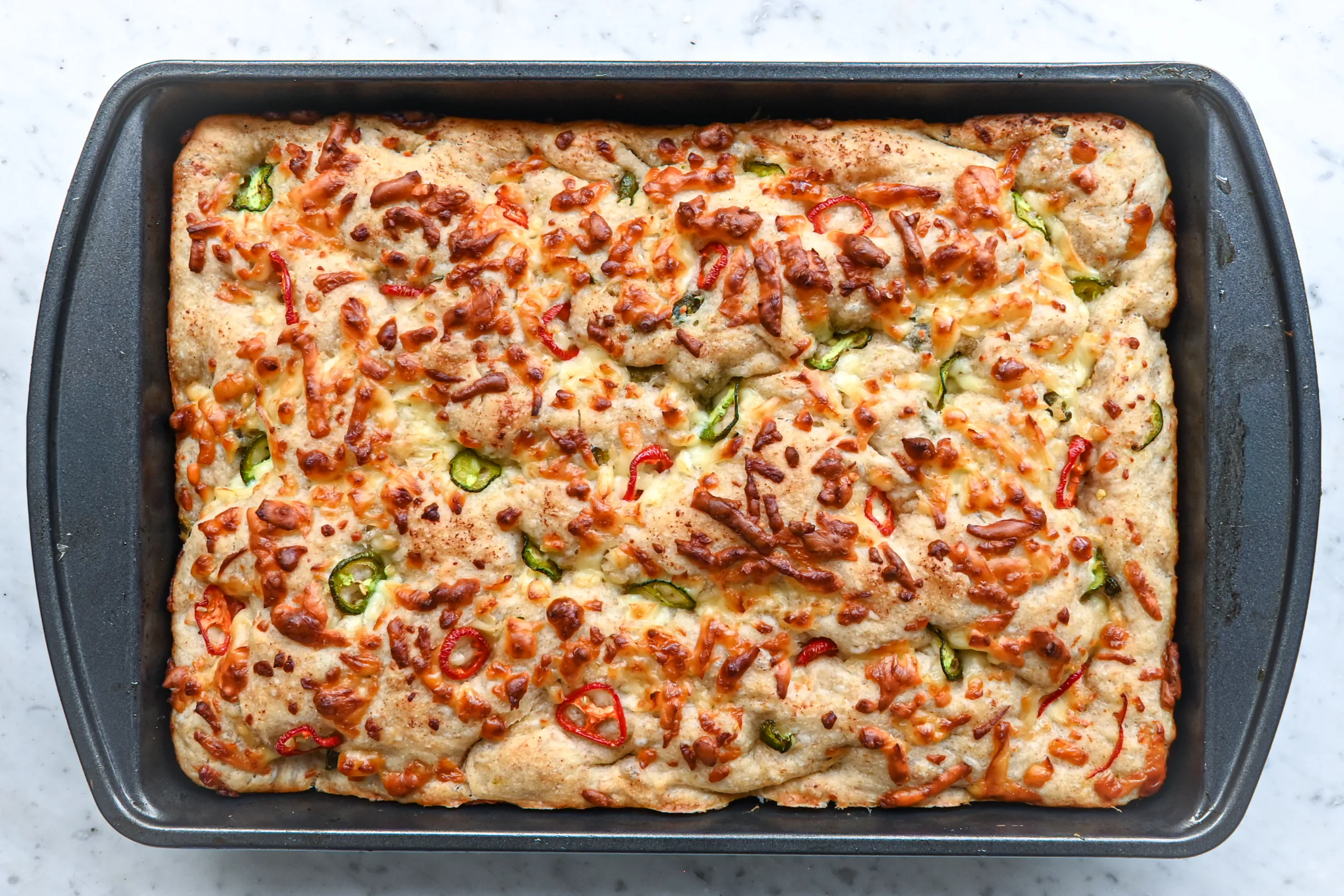 Jalapeño cheddar sourdough focaccia baked in a 9x13-inch pan with golden cheese and sliced peppers on top.