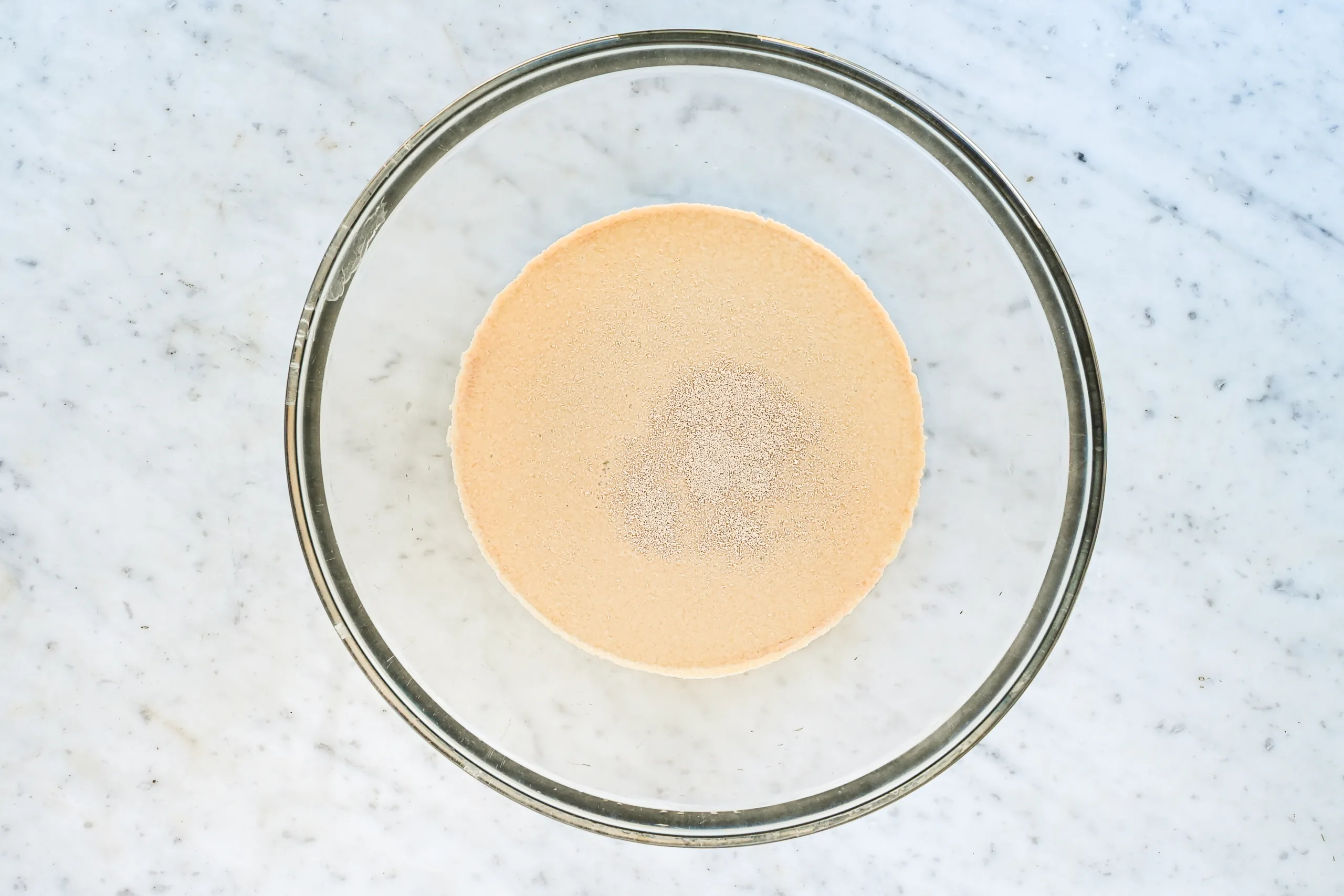 Active dry yeast blooming in warm water and sugar in a glass mixing bowl.