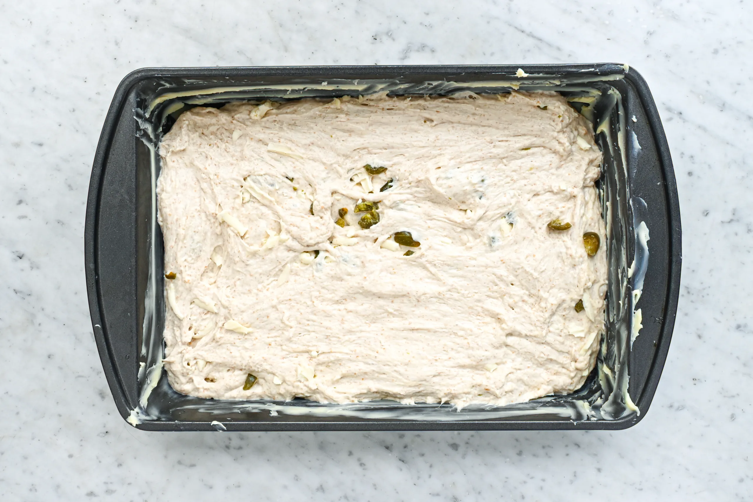 Jalapeño cheddar sourdough focaccia dough spread into a buttered 9x13-inch baking pan.