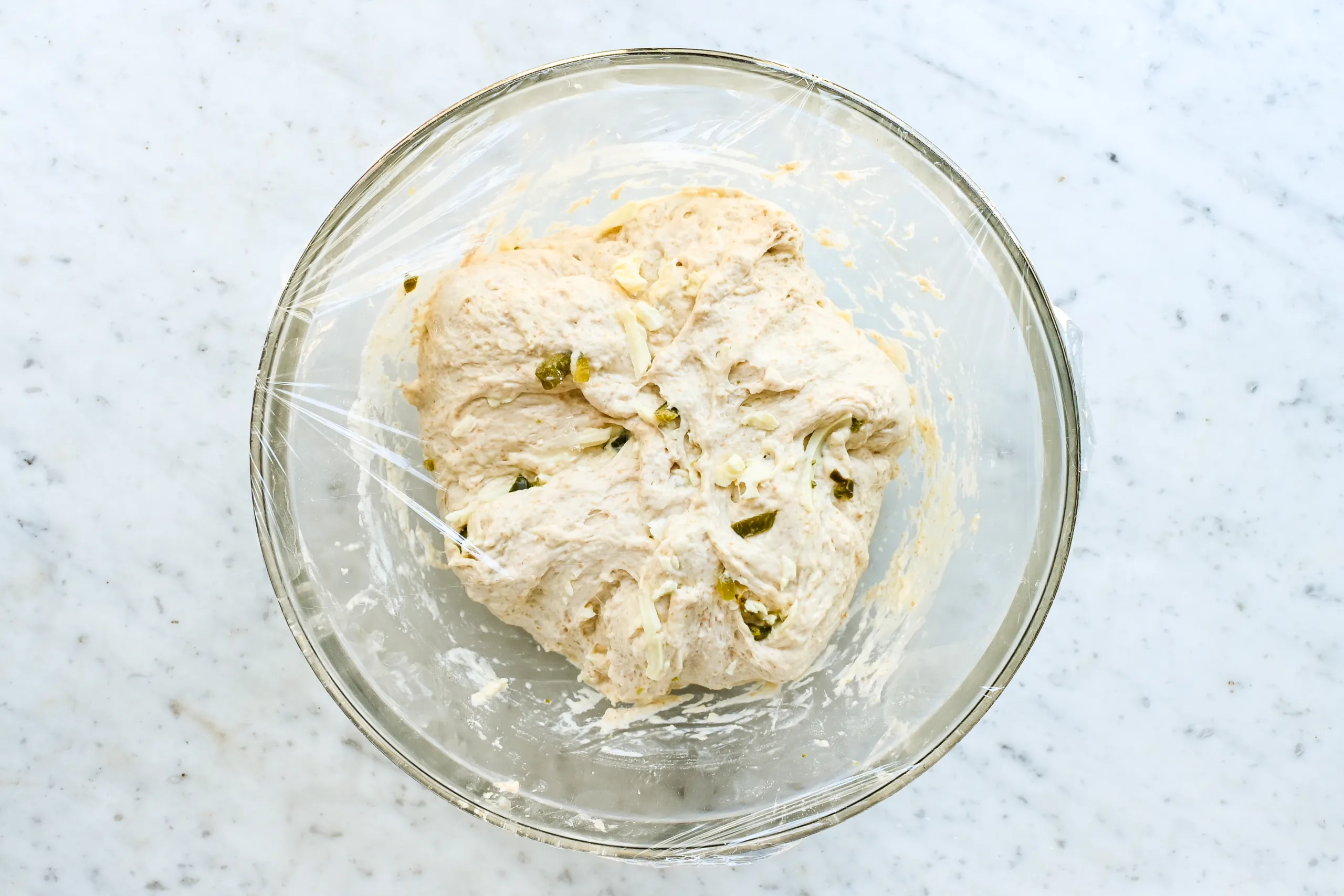 Jalapeño cheddar sourdough focaccia dough covered with plastic wrap for rising.