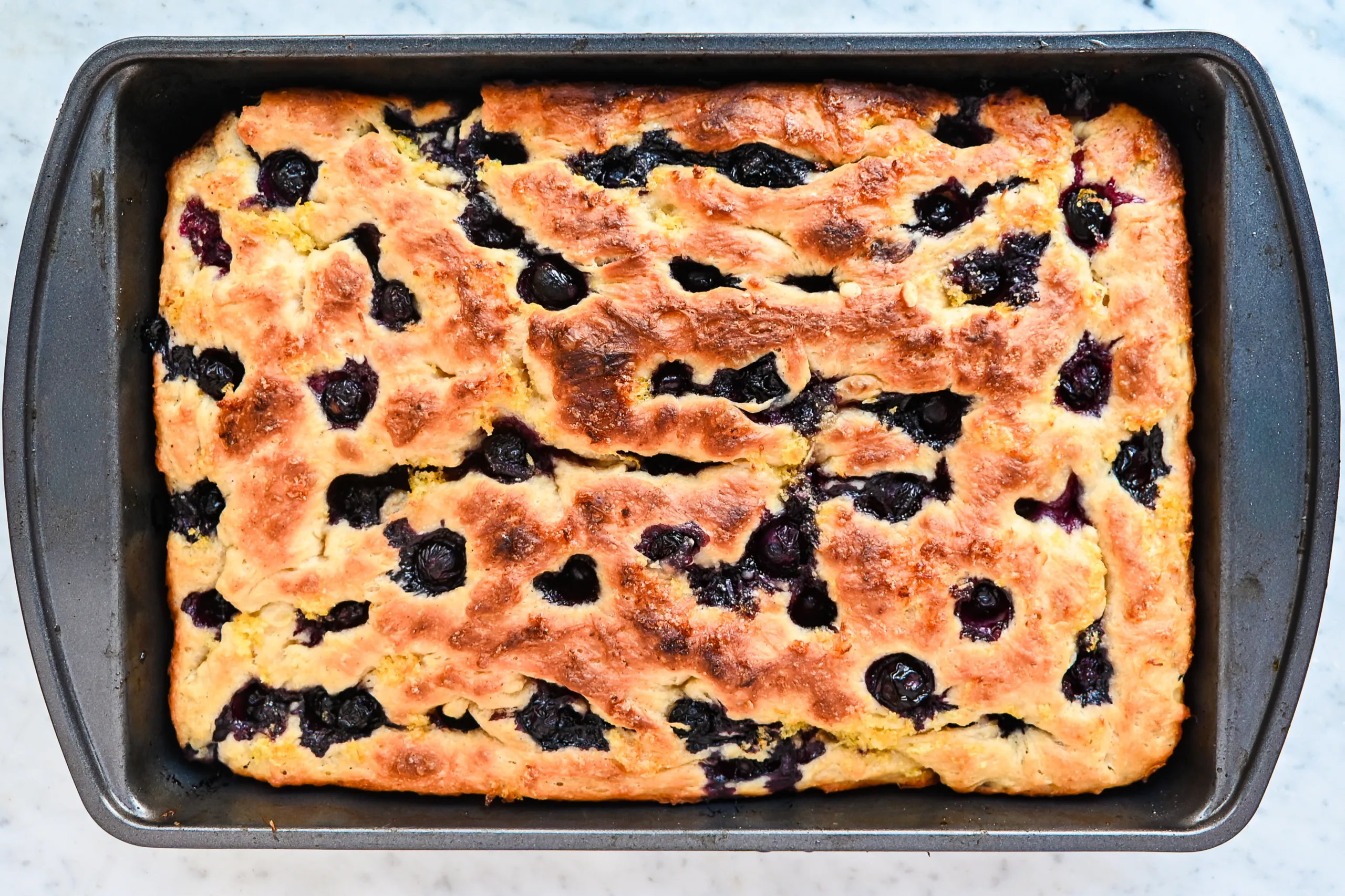 Baked lemon blueberry sourdough focaccia in a 9x13-inch pan with golden edges and blueberries throughout.