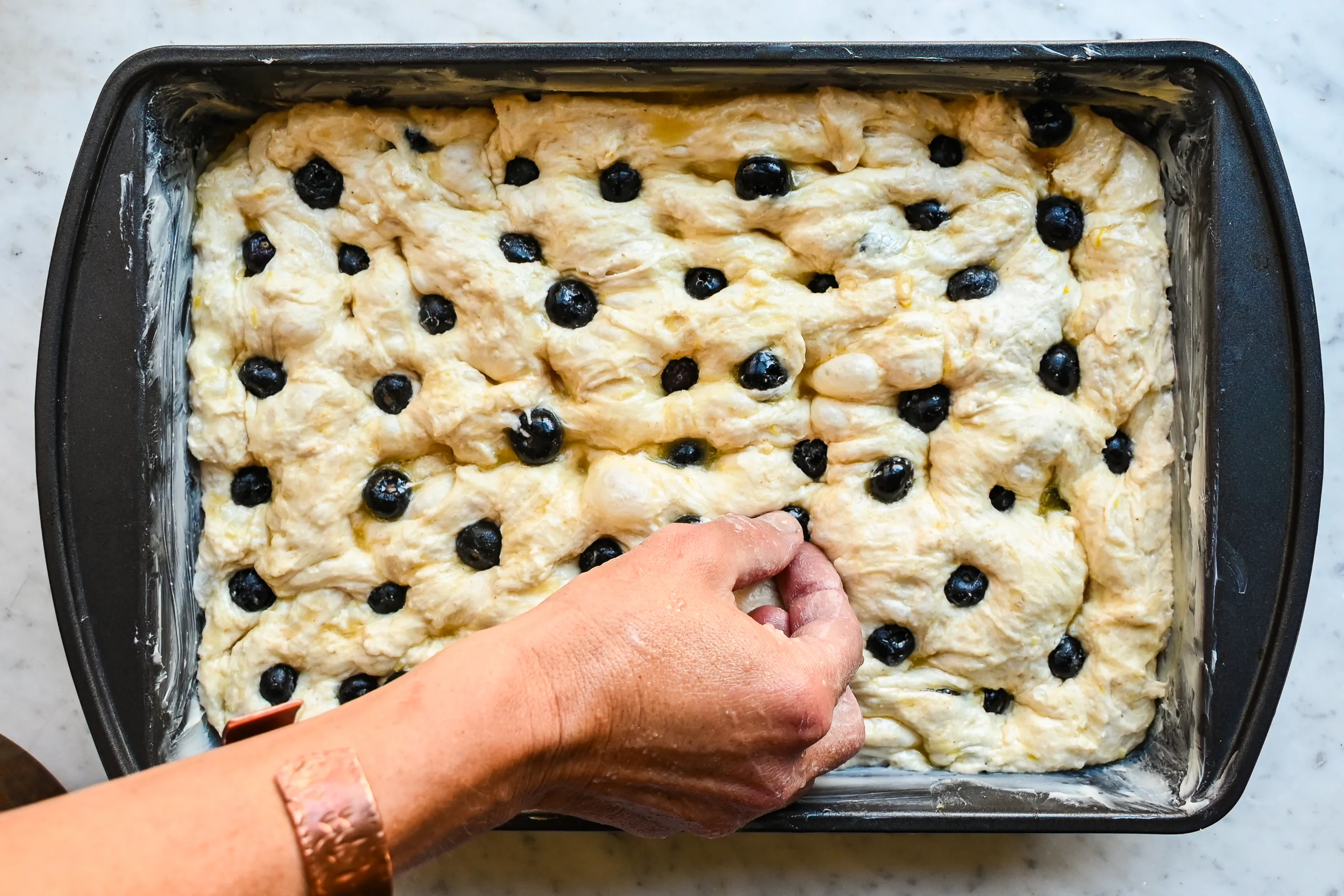 Unbaked lemon blueberry sourdough focaccia topped with fresh blueberries and lemon sugar before baking.