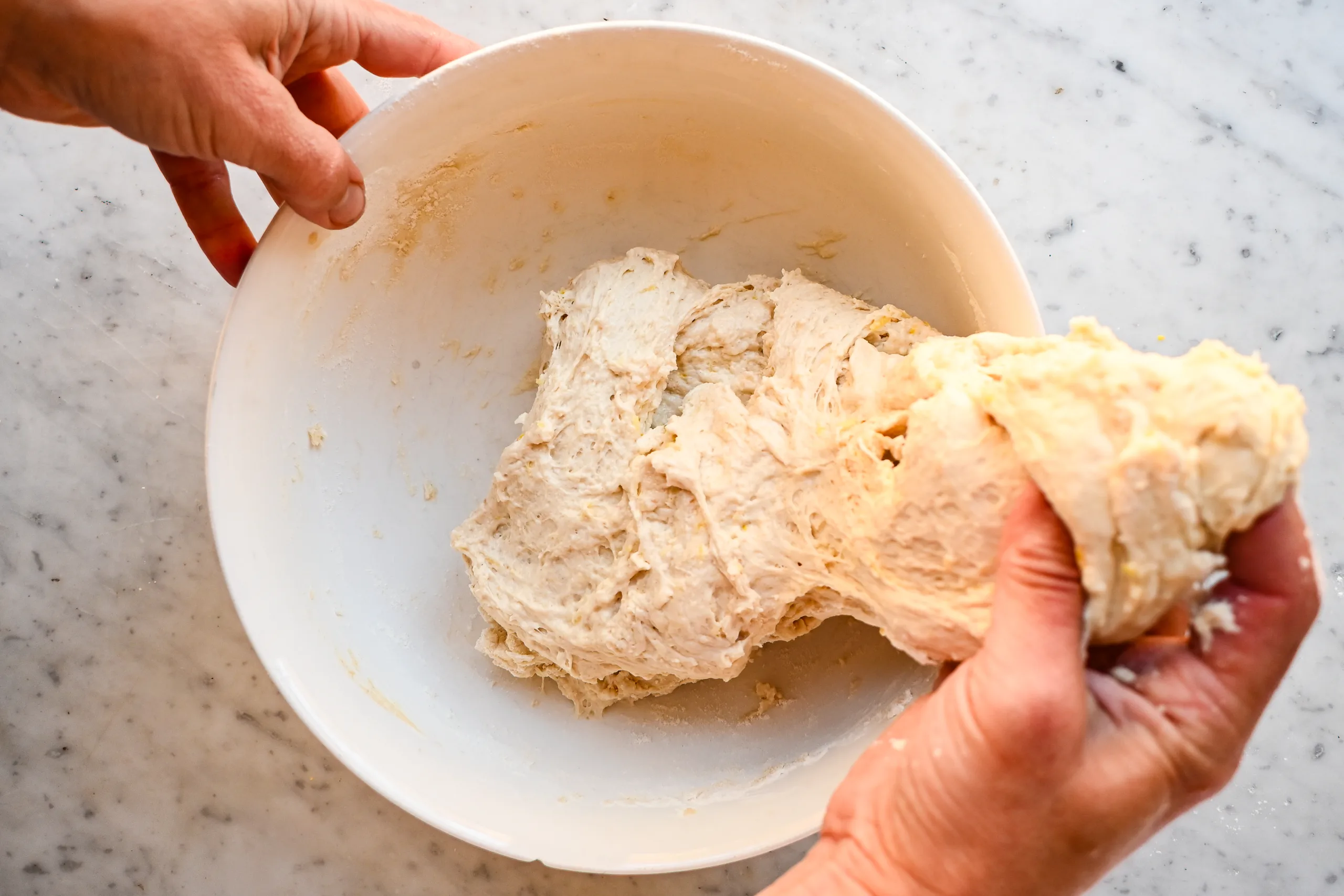 Stretching and folding lemon blueberry sourdough focaccia dough in a white mixing bowl.