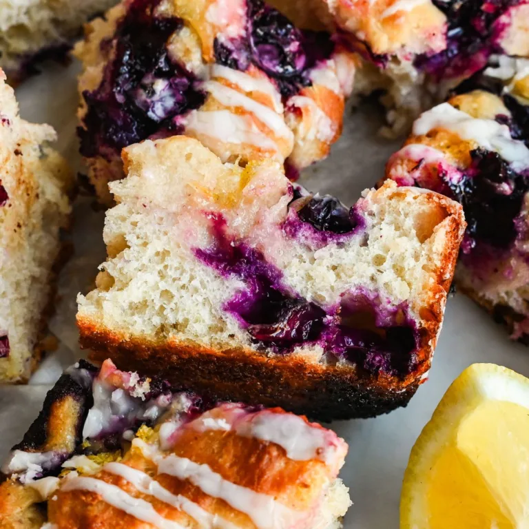 Sliced lemon blueberry sourdough focaccia showing the soft airy crumb, juicy blueberries, golden crust, and lemon glaze.