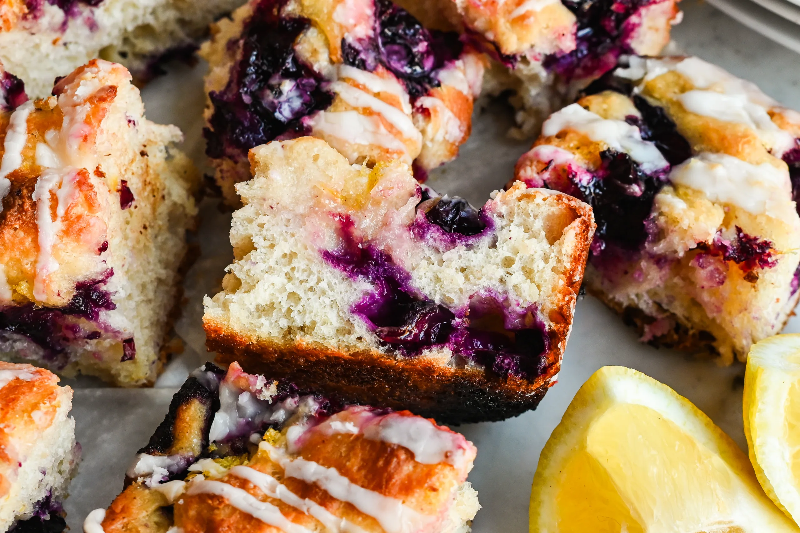 Sliced lemon blueberry sourdough focaccia showing the soft crumb, juicy blueberries, and lemon glaze.