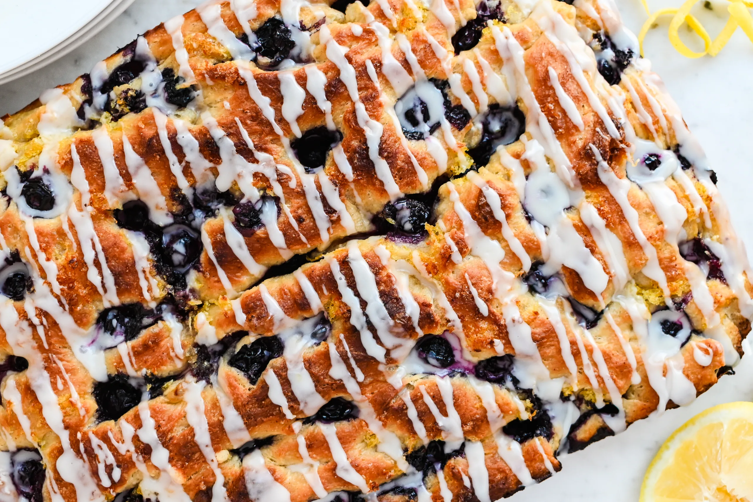 Lemon blueberry sourdough focaccia topped with a white lemon glaze and fresh blueberries.