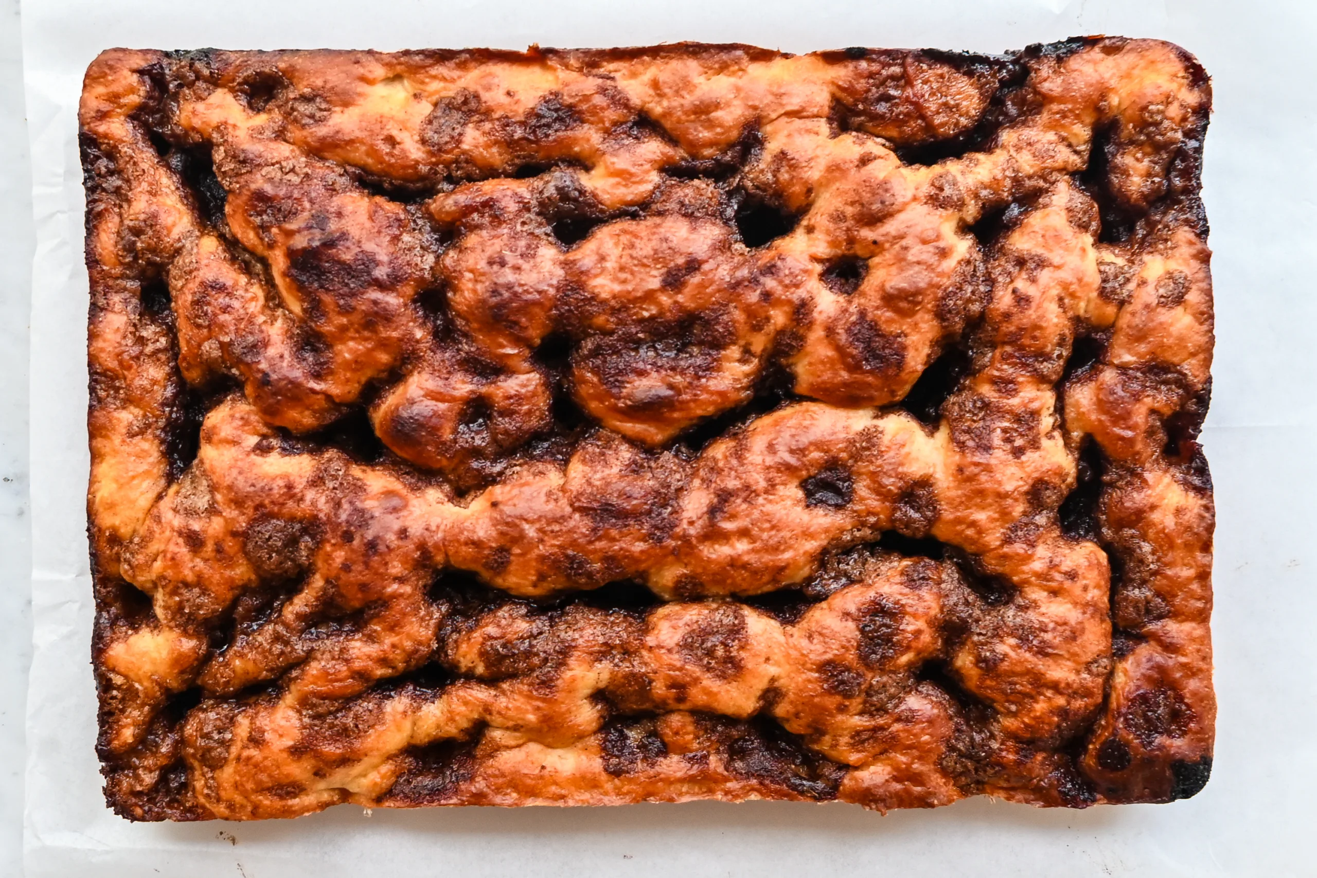 Baked cinnamon roll focaccia before glazing, with golden brown edges and cinnamon sugar pockets.