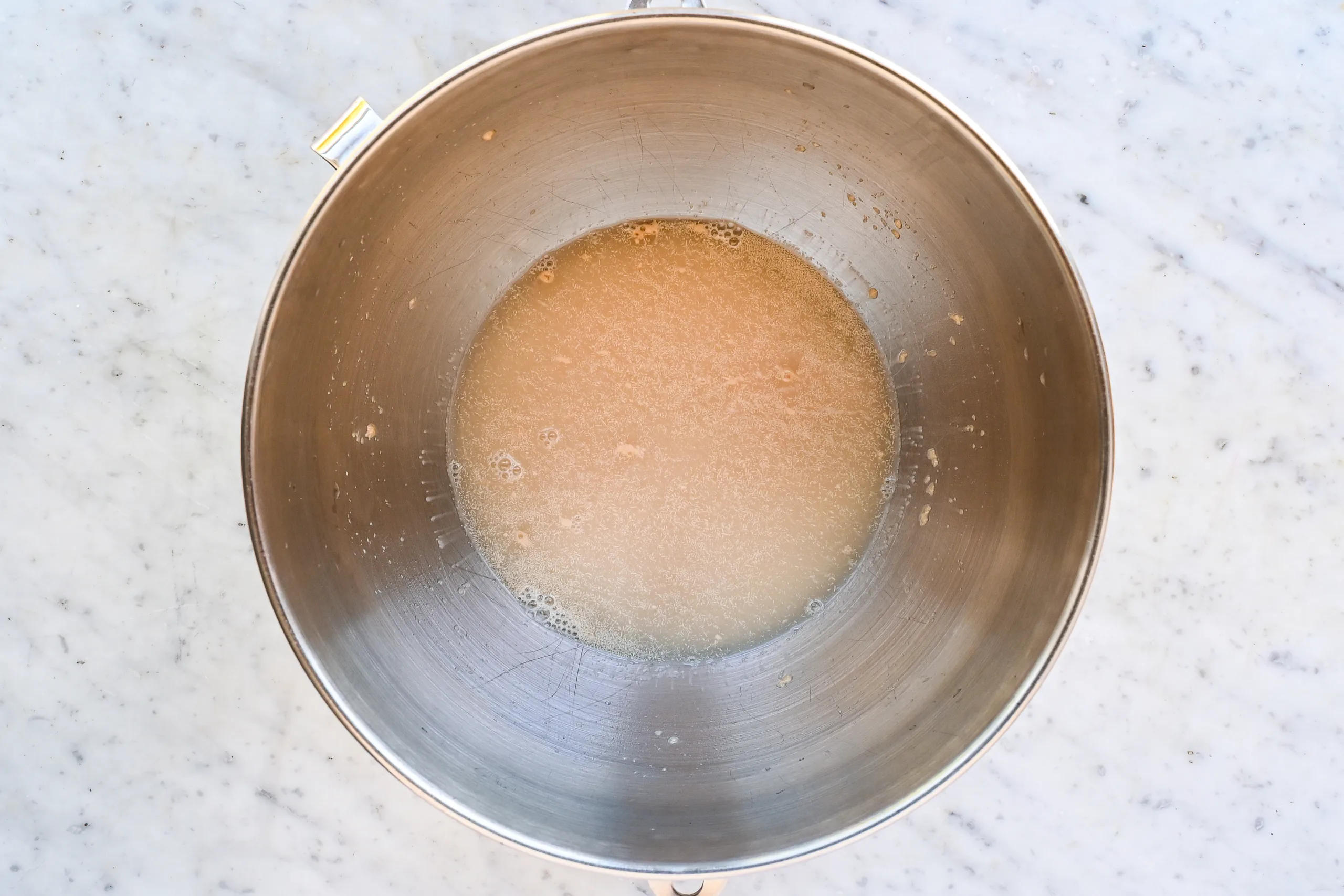 Warm water, sugar, and yeast in a stand mixer bowl for cinnamon roll focaccia dough.