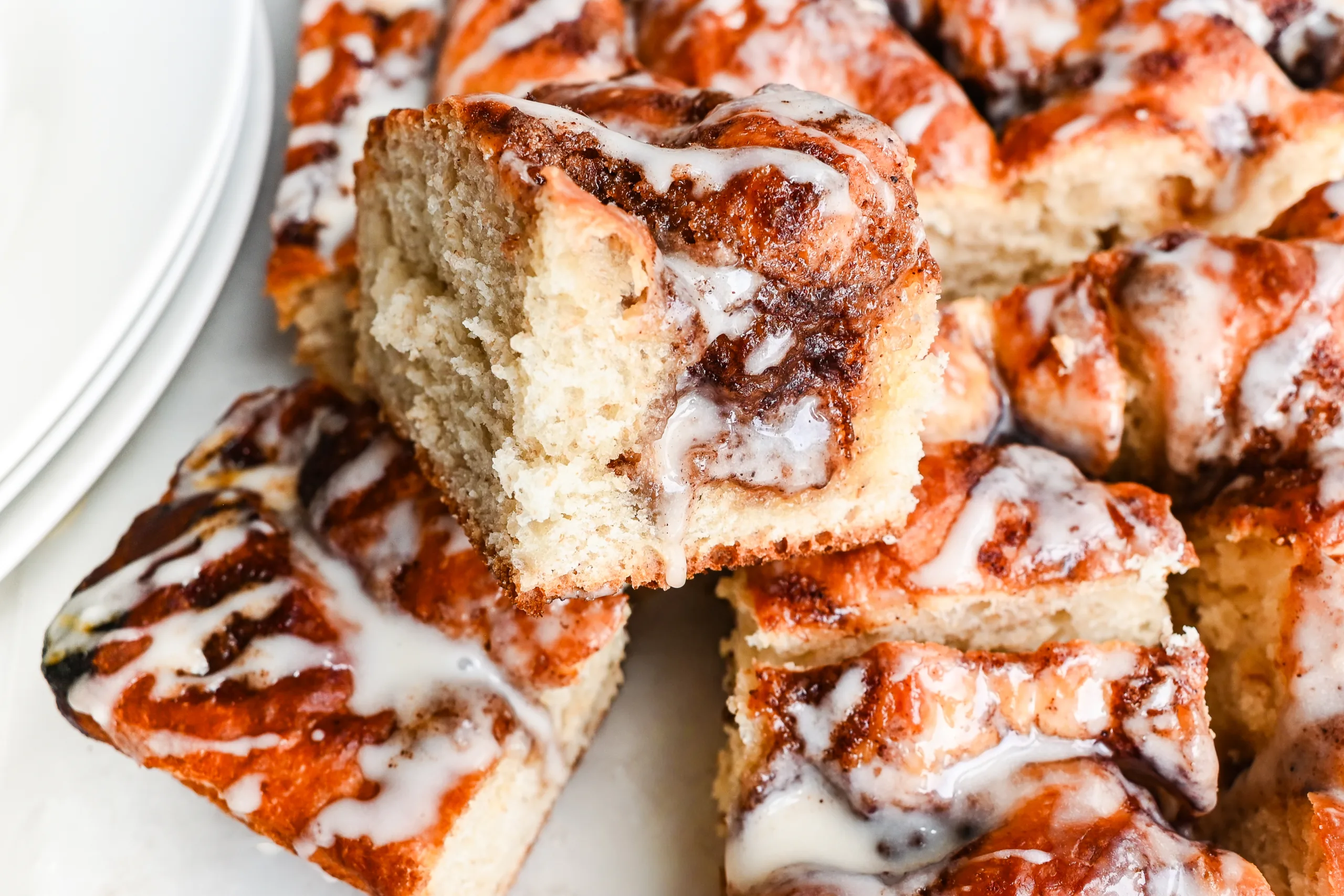 A piece of sourdough cinnamon roll focaccia lifted from the pan, showing the fluffy inside and glazed cinnamon topping.