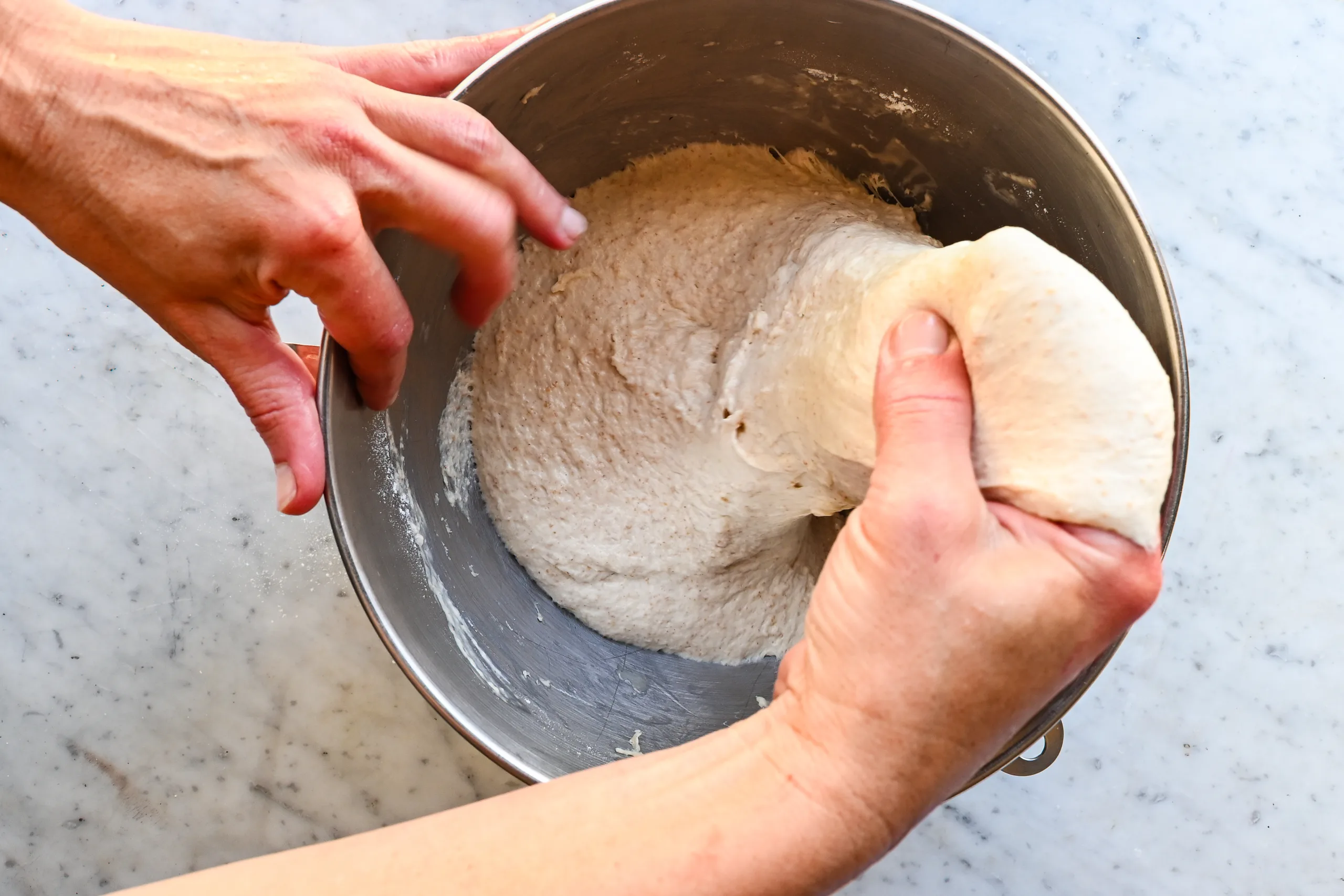 Sourdough focaccia dough being stretched into a buttered 9x13-inch baking pan.